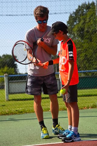 Entraineur de tennis apprenant au jeune à jouer  en colonie de vacances multisports au printemps