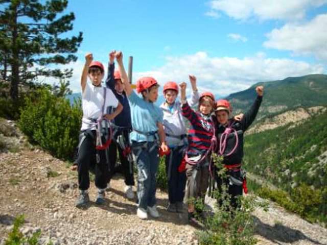 Groupe d'enfants victorieux au sommet d'une montagne après l'activité escalade en colonie de vacances au printemps 