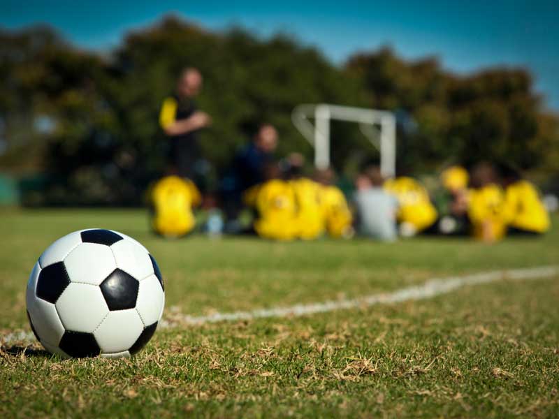 Ballon de football et groupe d'adolescents qui écoute l'entraineur de football