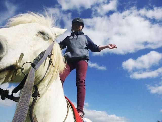 Enfant debout sur son cheval en colonie de vacances équitation