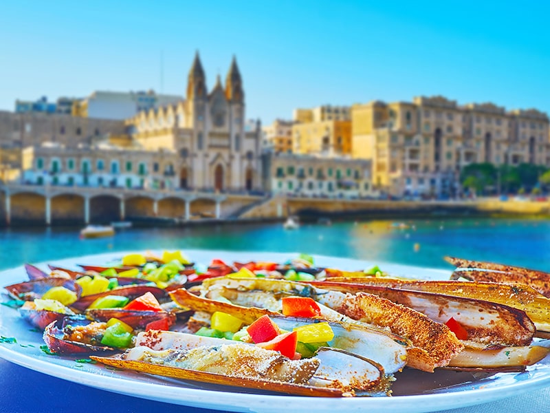 Vue sur les bateaux de Malte avec un plat typique en premier plan lors d'une colonie de vacances linguistique à Malte