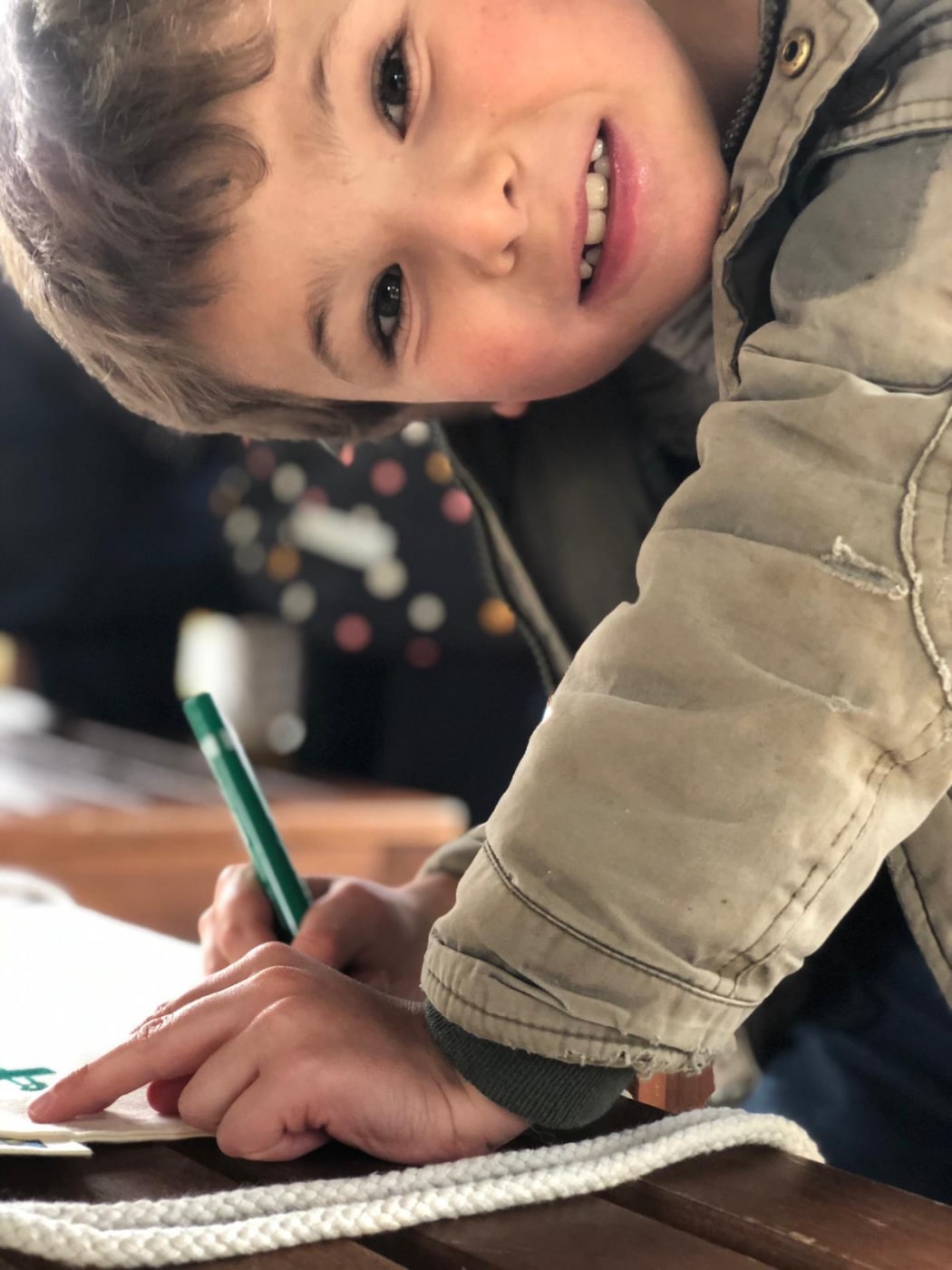Vue sur un jeune garçon avec un grand sourire qui dessine et peint sur un sac en toile lors de sa colonie de vacances Artistes en herbe