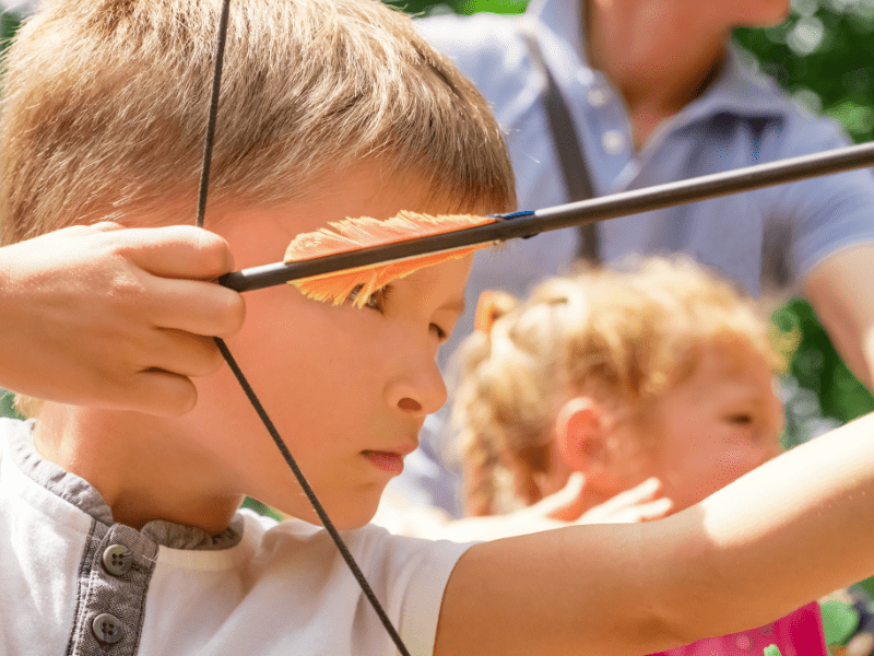 Enfant qui fait du tir à l'arc durant sa colo de vacances Montagne Nature à Paques