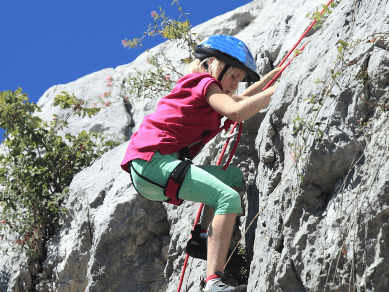 Jeune fille qui grimpe une falaise en colo de vacances Sciences and Fun au printemps