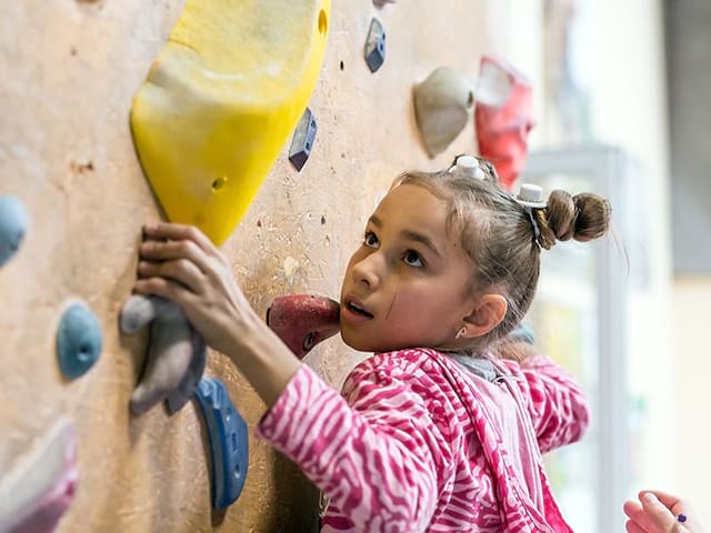 Jeune fille qui grimpe un mur d'escalade en colo de vacances Escalade et Trampoline ce printemps