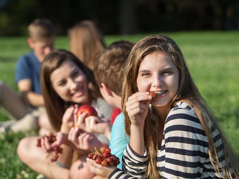 Enfants et ados qui font un pique-nique dans l'herbe durant une colonie de vacances Corps et Esprit 