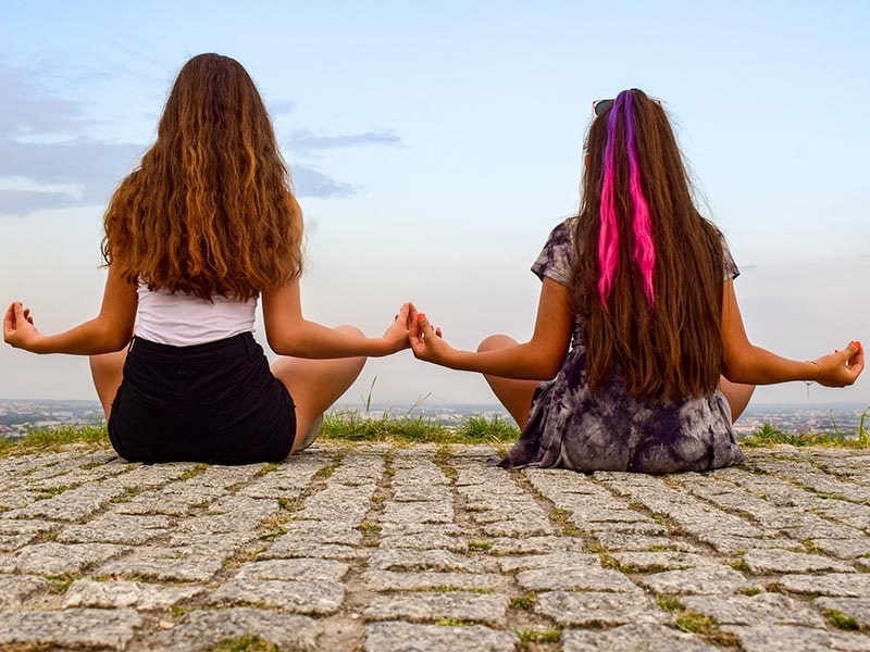 Vue sur deux jeunes filles de dos en position yoga lors d'une colonie de vacances Corps et Esprit durant le printemps