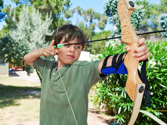 Enfant de 10 ans faisant du tir à l'arc en colonie de vacances à la campagne