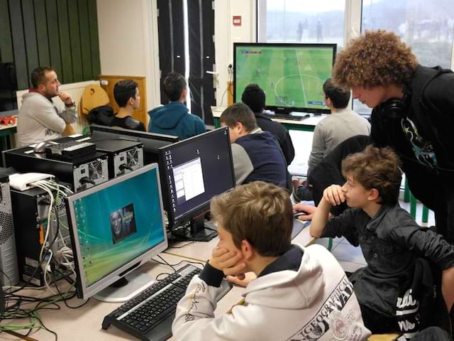 enfants et leur animatrice jouant aux jeux vidéo en colonie de vacances pour geek à la montagne