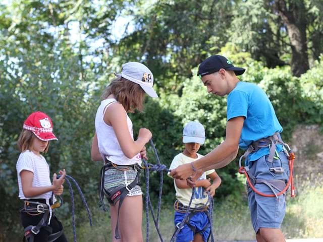 enfants apprenant à mettre leur baudrier pour faire de l'escalade en colonie de vacances 