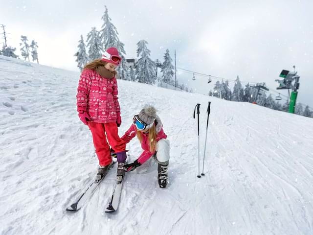 enfants apprenant à chausser les skis en colonie de vacances à la montagne