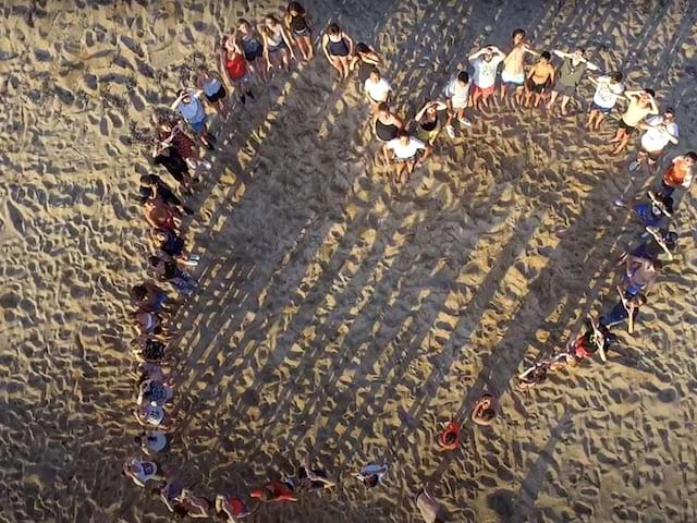 Groupe d'enfants formant un coeur sur la plage en colo en corse