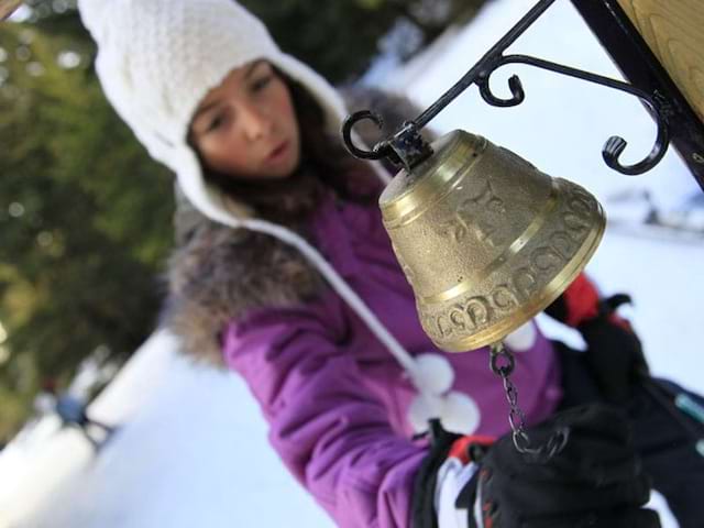 Jeune fille jouant avec la cloche d'un chalet en colonie de vacances à la neige