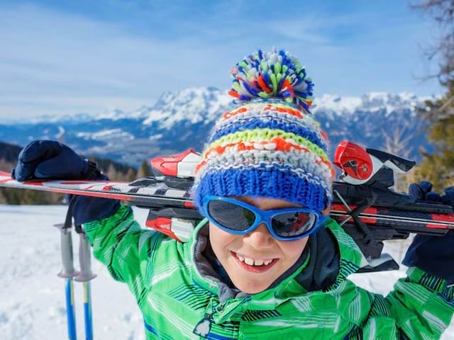 Portrait d'un jeune garçon sur les pistes de ski portant ses ski sur ses épaules en colo