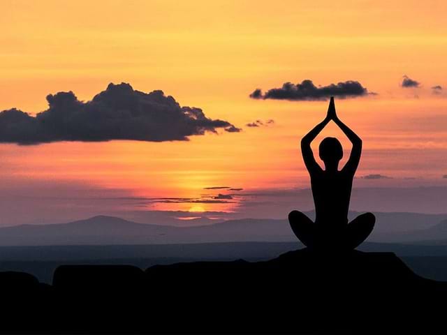 Jeune femme faisant du yoga devant un coucher de soleil en colo 