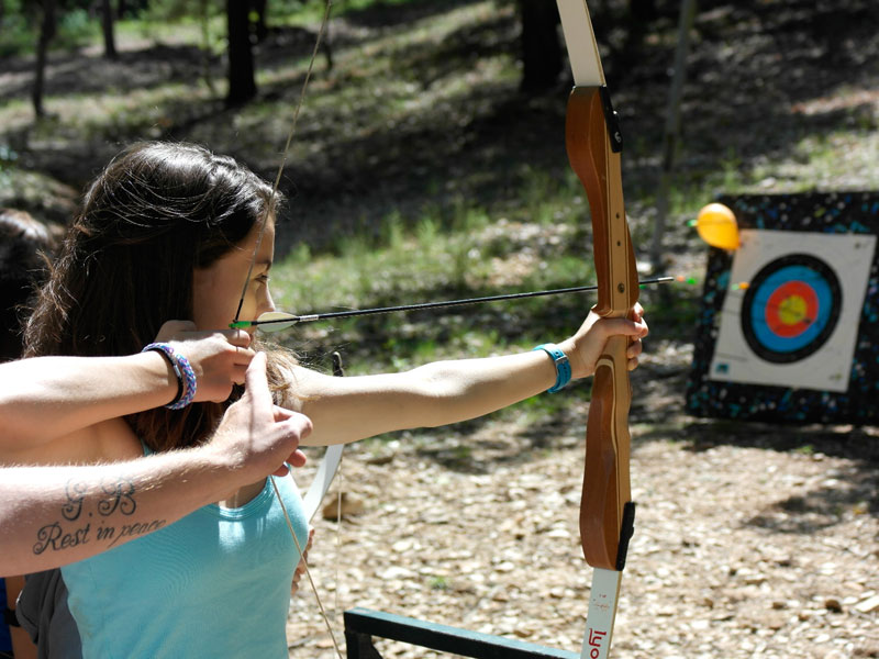 Adolescente de 14 ans apprenant à faire du tir à l'arc avec son animatrice de colo