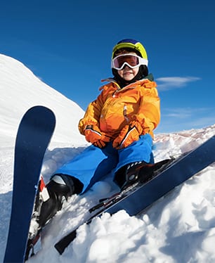 Jeune enfant débutant au ski en colonie de vacances ski assis dans la neige