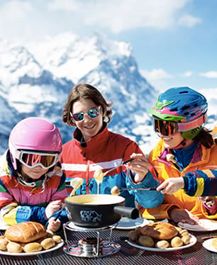 Groupe d'enfants et ados mangeant une fondue savoyarde cet hiver en colonie de vacances ski