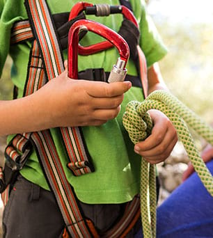 Enfant apprenant à utiliser les mousquetons de via ferrata en colo