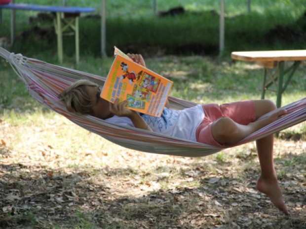 Enfant en colonie de vacances qui se repose et lit un magazine dans un hamac