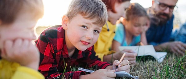 Enfants en classe découverte prenant des notes dans l'herbe