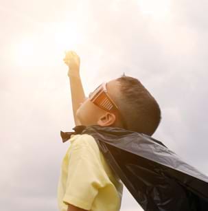 Jeune garçon avec une cape qui tend le bras vers le ciel tel un superhéros