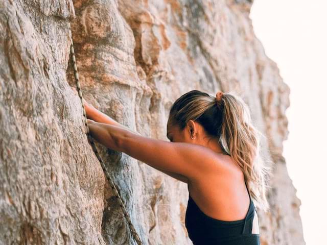 Ado qui escalade une falaise lors d'une initiation en colo de vacances à Pâques