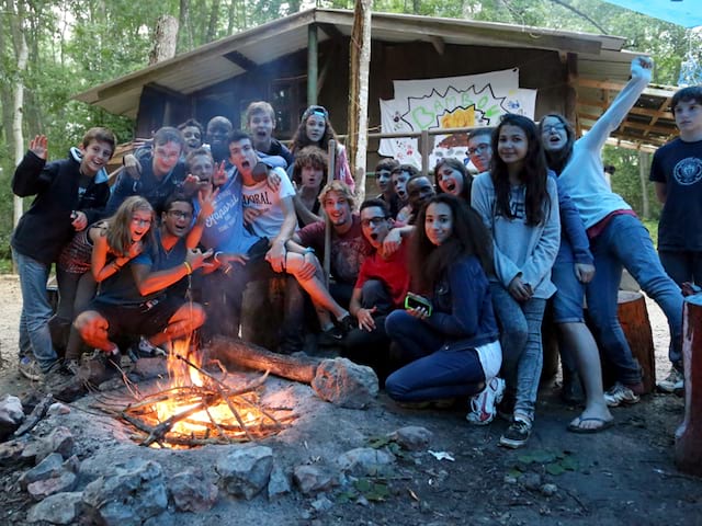 groupe d'ados et enfants autour d'un feu de camp en colo 