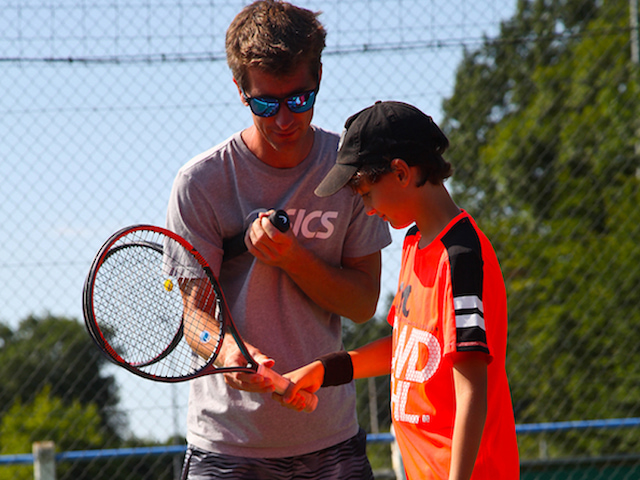 Animateur apprenant à un ado à manier la raquette de tennis