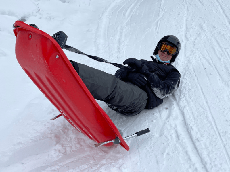 Jeune garçon de 14 ans qui est assis dans sa luge et qui profite de sa colo de vacances au ski cet hiver