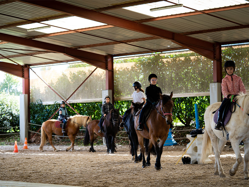 Enfants et leurs chevaux qui font des tours de manège lors d'une colo de vacances hivernale d'équitation