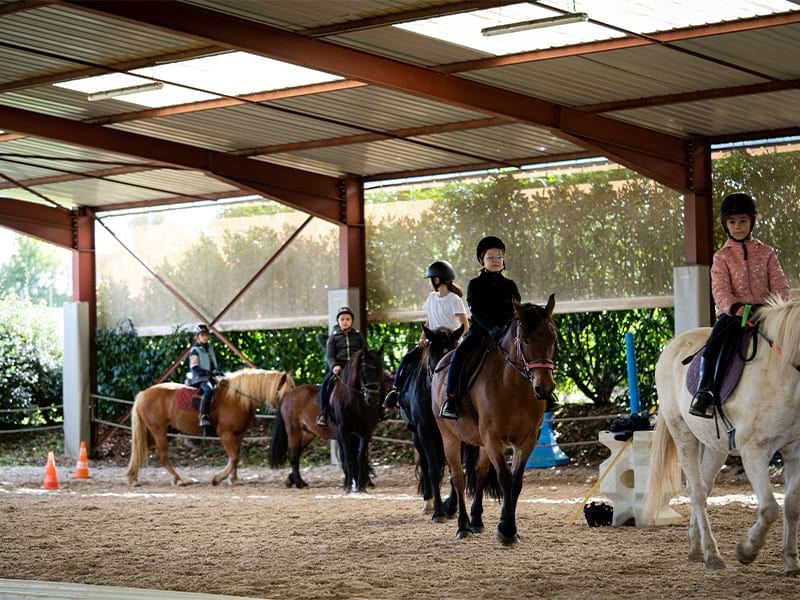 Enfants et leurs chevaux qui font des tours de manège lors d'une colo de vacances hivernale d'équitation