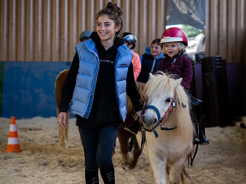 Monitrice et enfant qui pratiquent l'équitation lors d'une colo de vacances de l'hiver