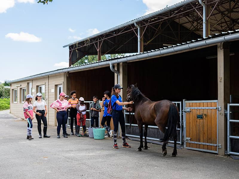 Vue sur les box des chevaux avec une monitrice et les enfants lors d'une colo de vacances du printemps