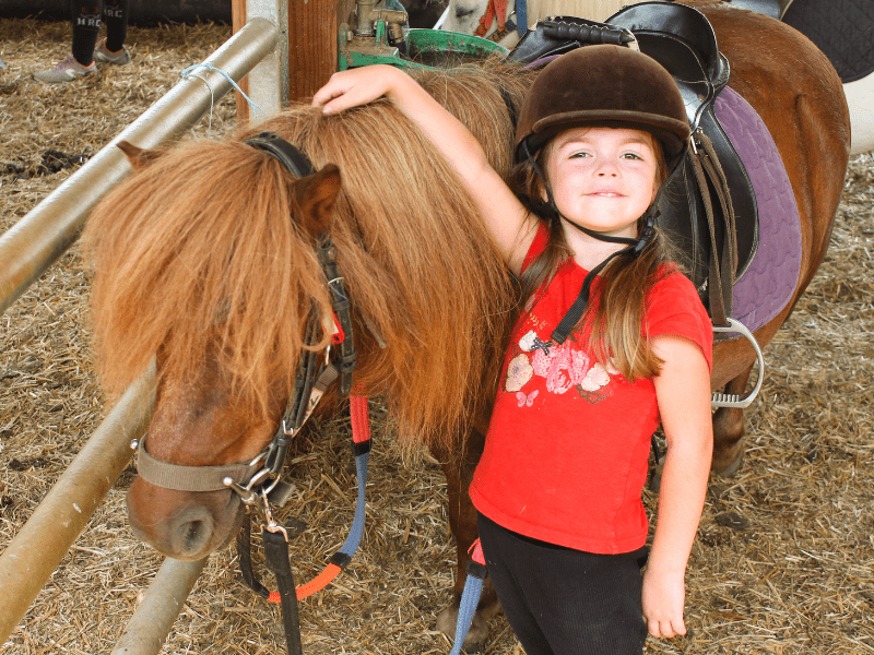 Enfant en colo de vacances qui s'occupe de son poney ce printemps