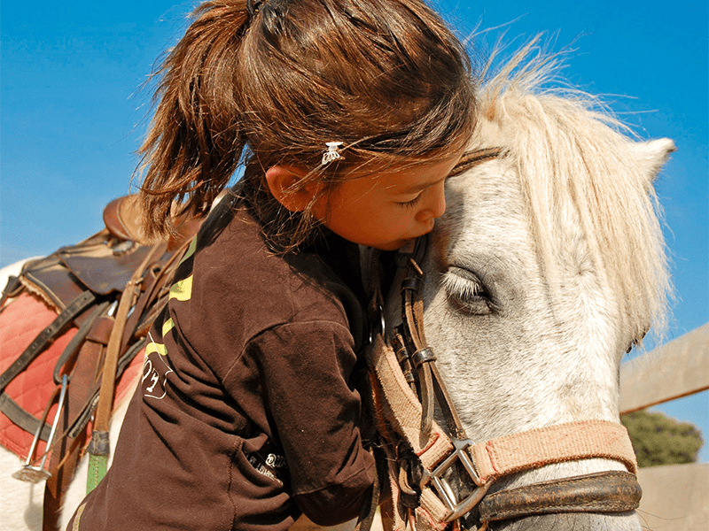 Jeune fille de 7 ans qui fait un calin à son poney après une séance d'équitation en colo de vacances cet automne