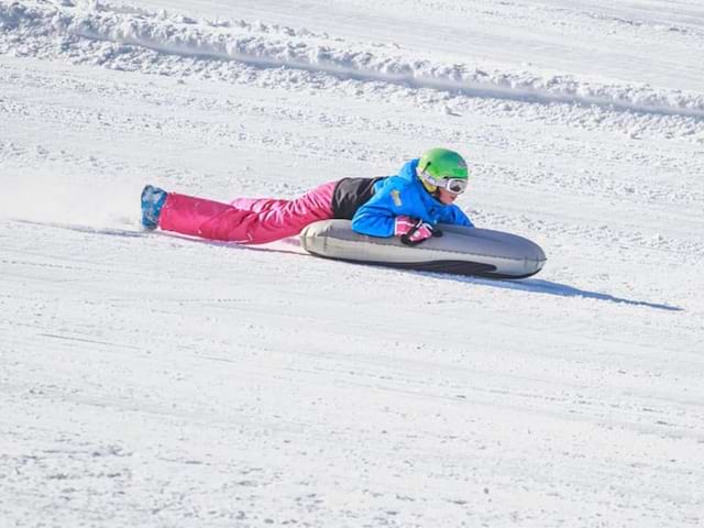 Jeune qui dévale les pistes en Airboard lors d'une colo de vacances hivernale 100% Adrénaline